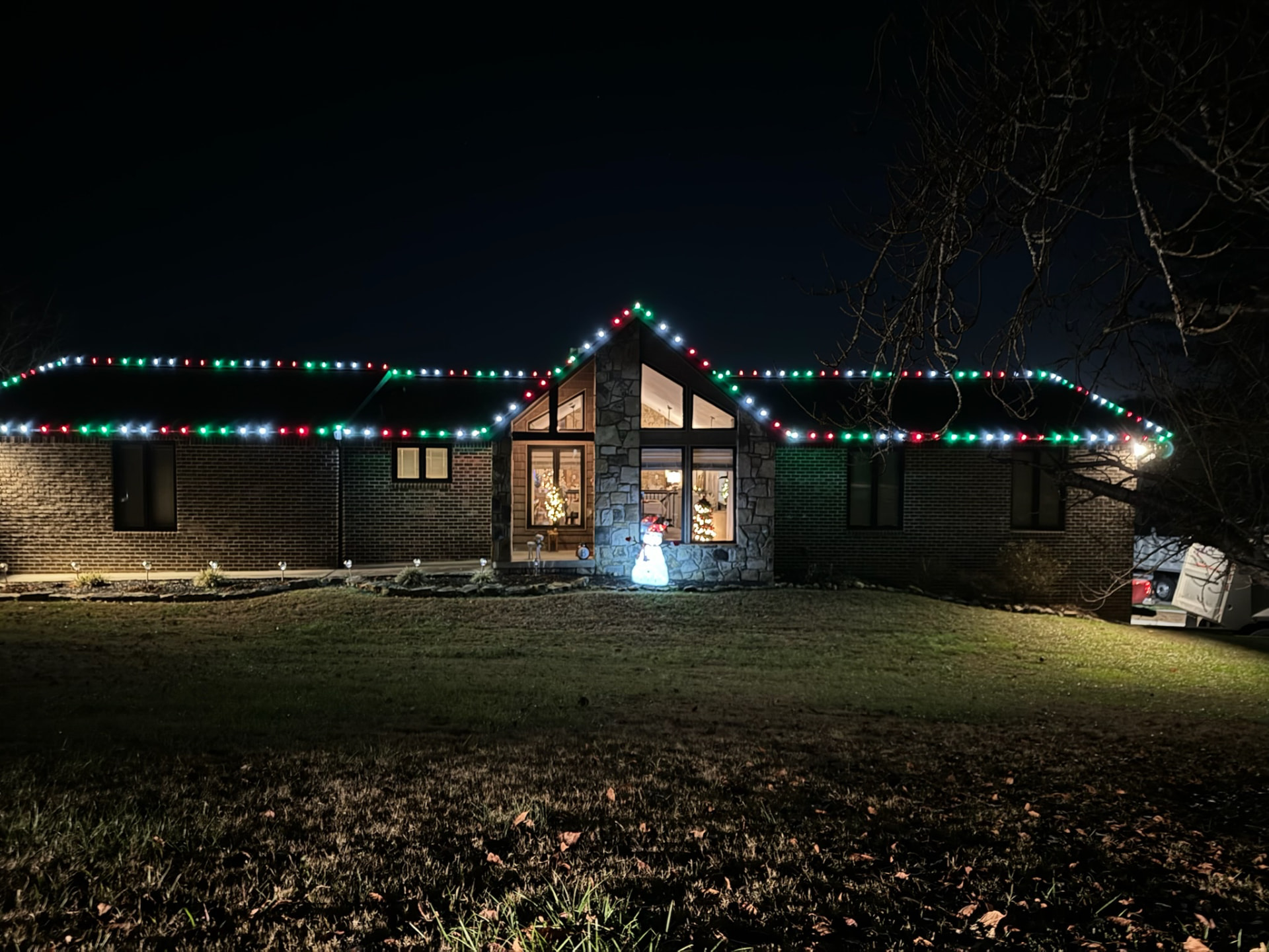 Brick and stone ranch home at night outlined in red green and white C9 Christmas lights across a long unbroken roofline
