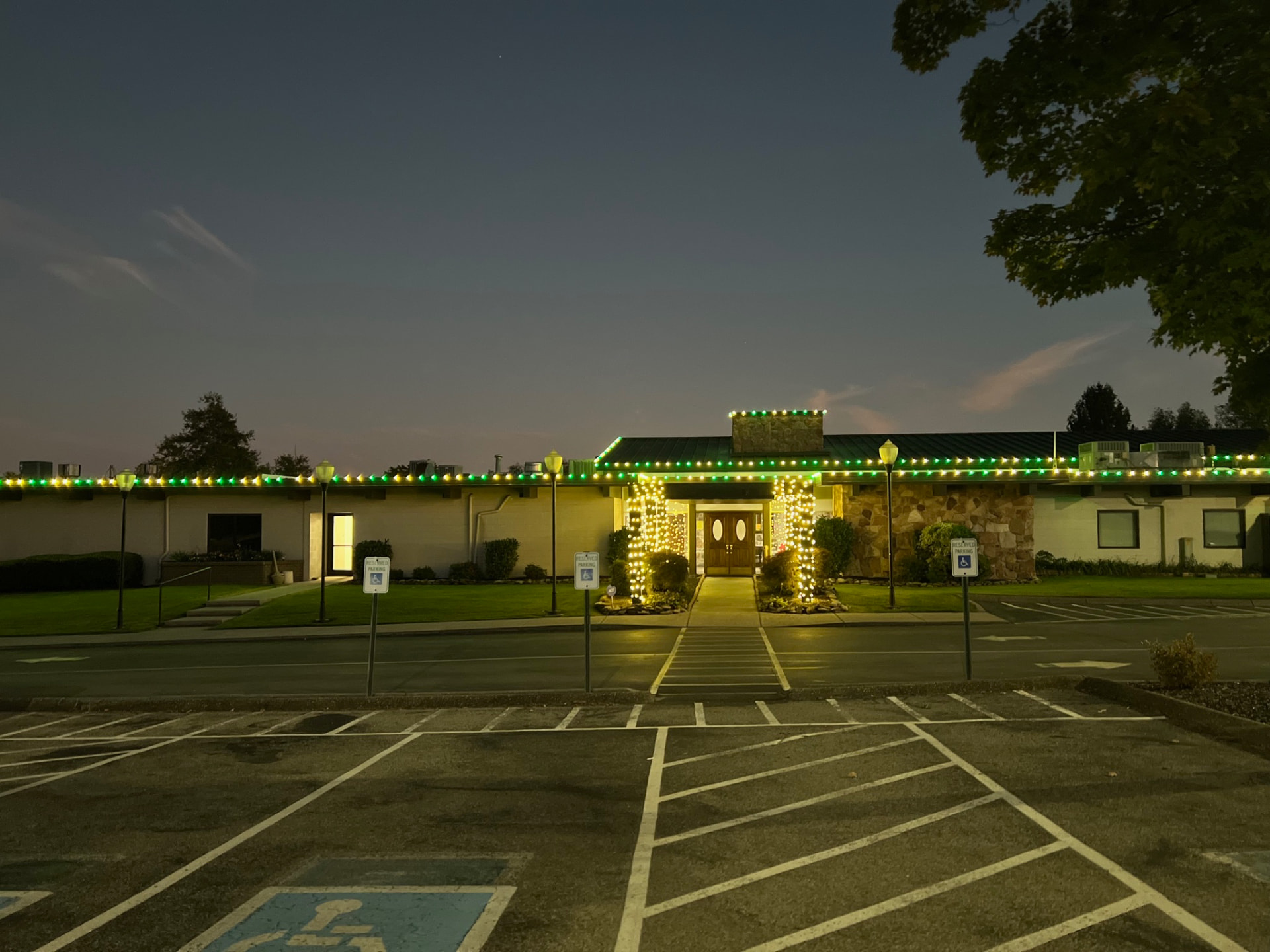 Commercial clubhouse building in Maryville TN lined with green and warm white C9 Christmas lights along the full roofline with lit entry columns