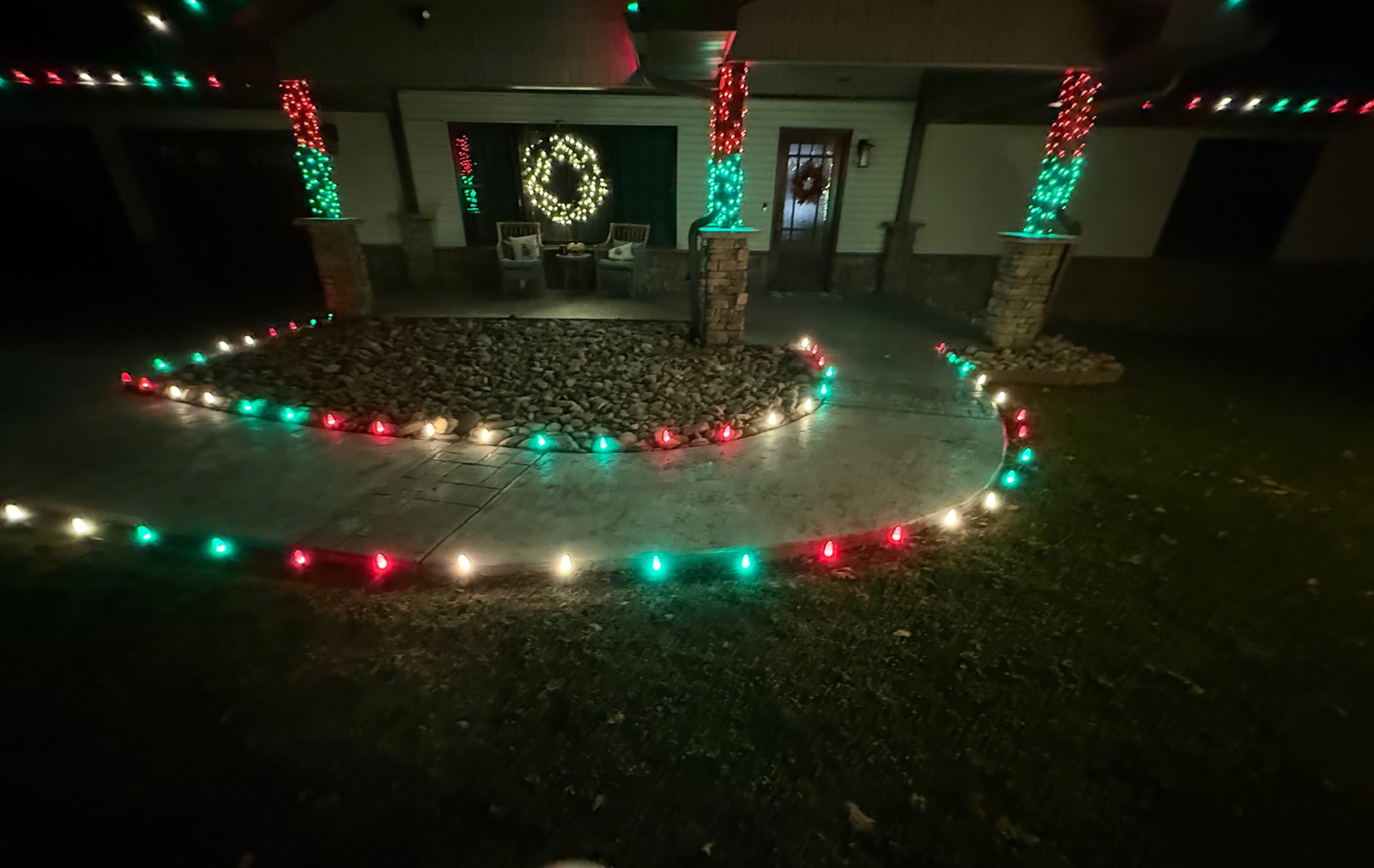 Front porch with red and green wrapped stone columns, an illuminated wreath on the door and red and green pathway bulbs