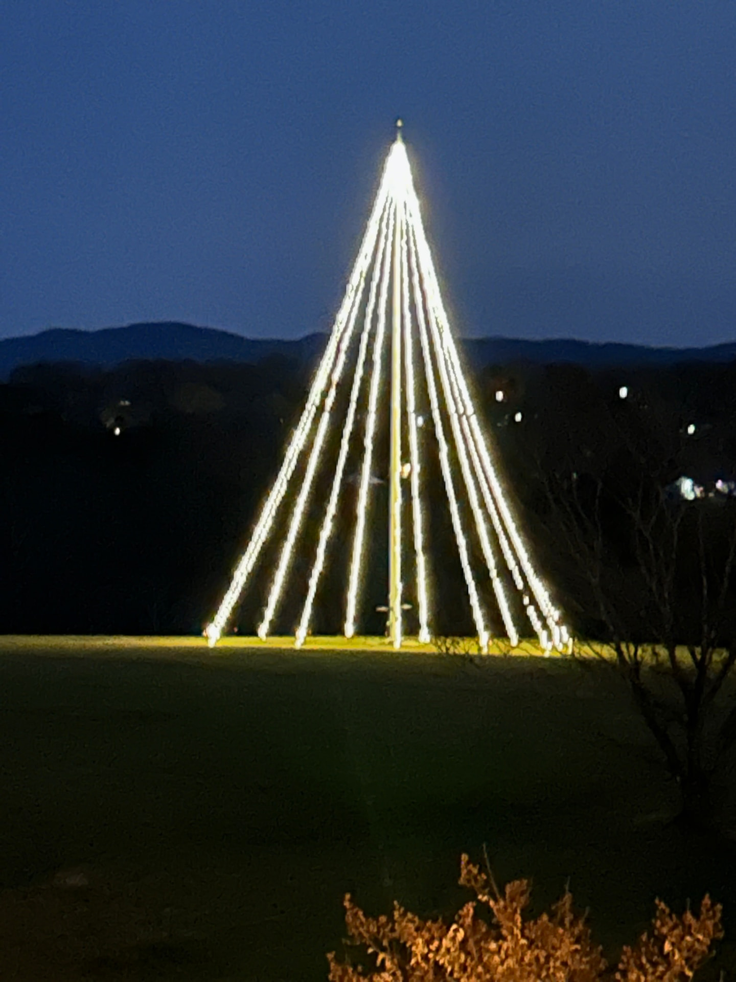 Tall warm white mega tree light display glowing on a hillside against the Smoky Mountains at dusk