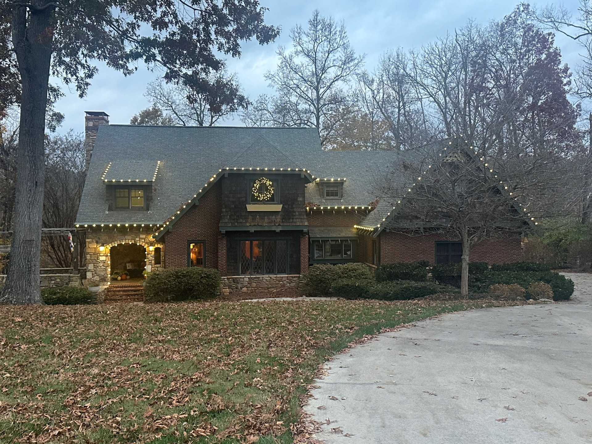 Brick and shingle cottage photographed in daylight showing Christmas light strands nearly invisible along the rooflines