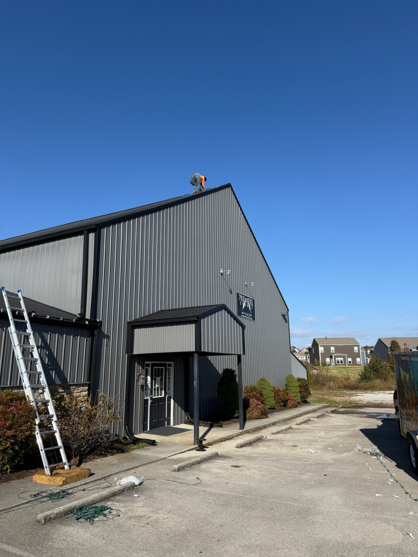 Installer on the roof edge of a commercial metal building attaching Christmas light strands during a daytime installation