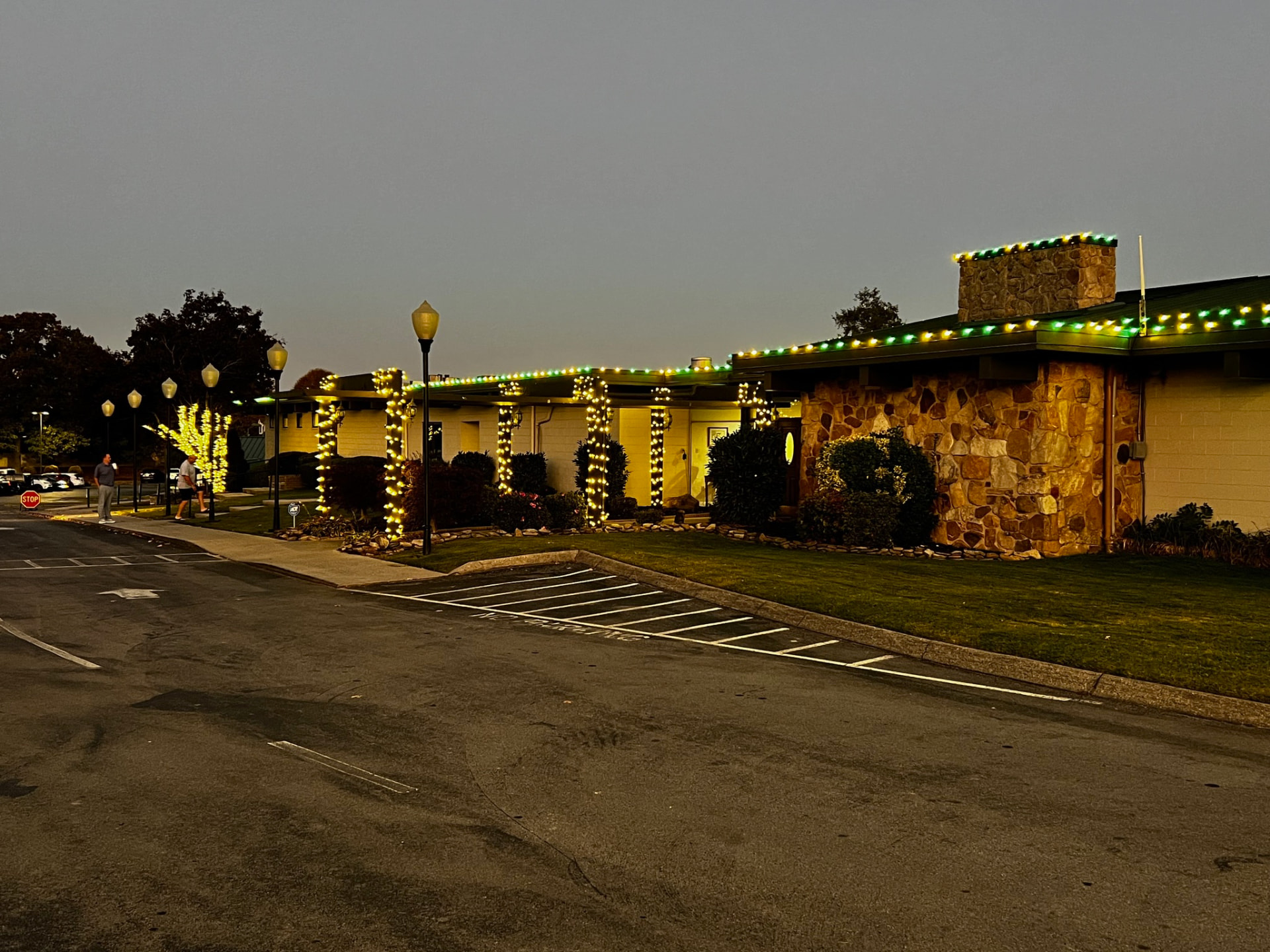 Commercial property at dusk with green and gold roofline lights and every walkway column wrapped in warm white mini lights