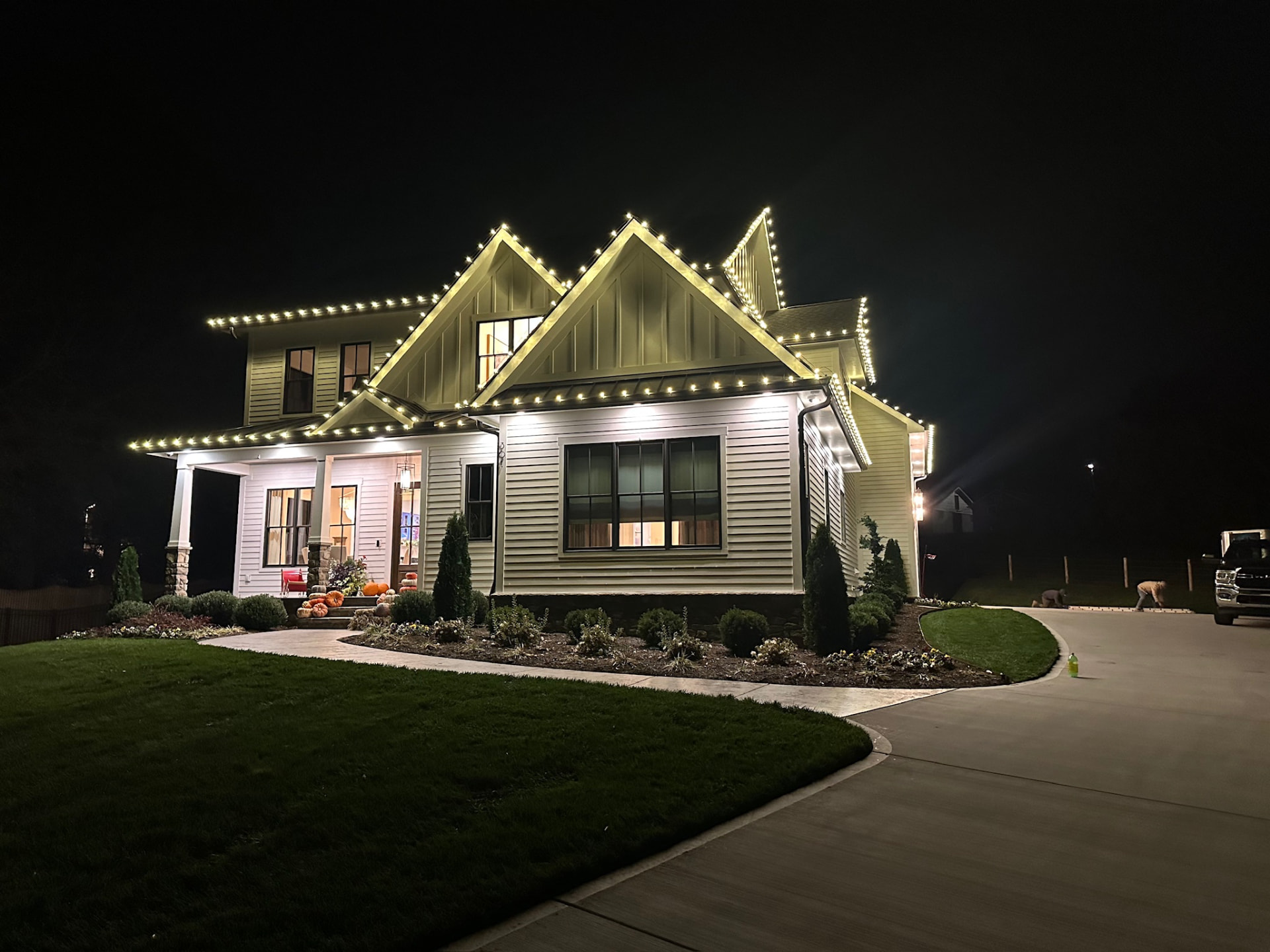 Modern farmhouse at night with warm white C9 Christmas lights outlining every gable, dormer and porch line