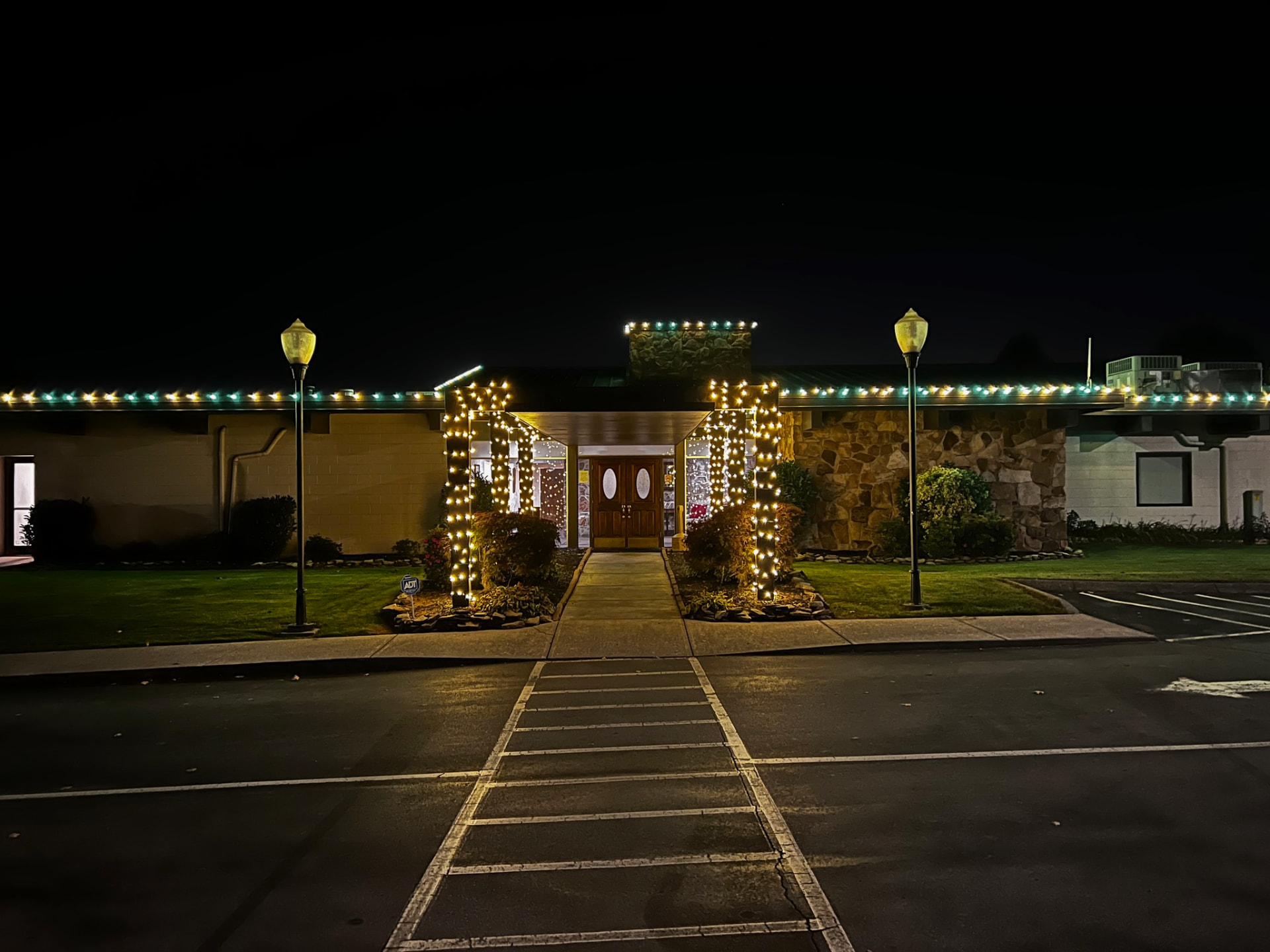 Church building at night with green and warm white C9 Christmas lights along the full roofline and lit entry columns framing the front doors