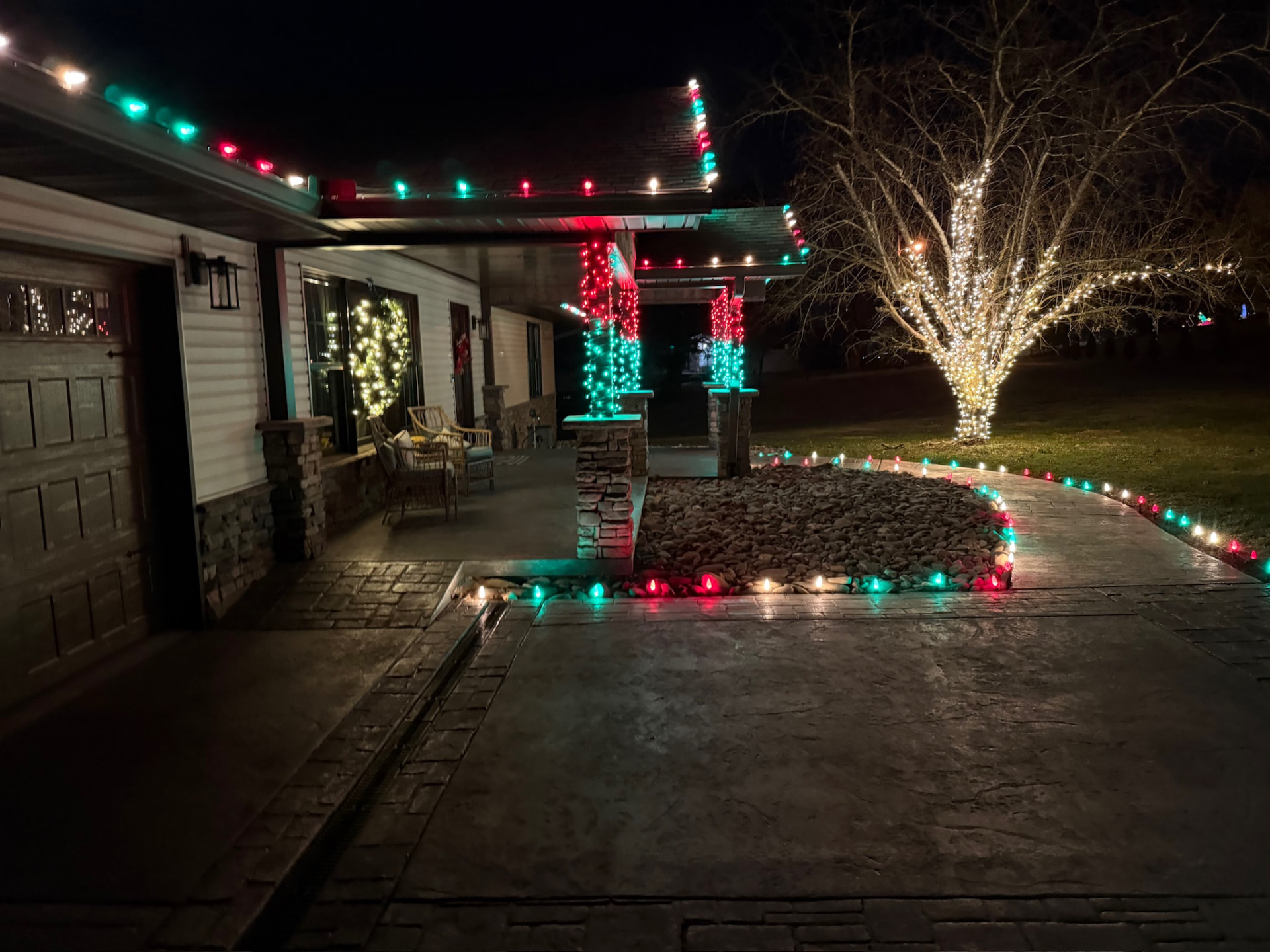 Stamped concrete driveway and walkway lined with red, green and white Christmas bulbs beside a lit covered porch