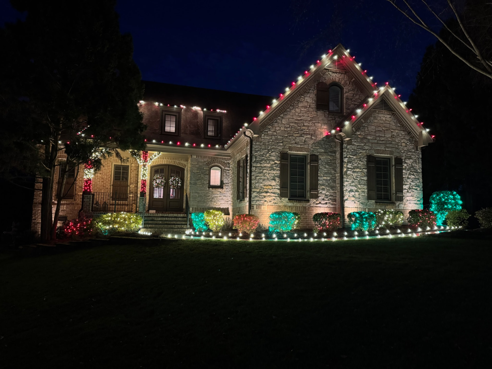 Stone and brick Maryville TN home at night with red and white C9 roofline lights, red and green net-lit shrubs and warm white pathway bulbs