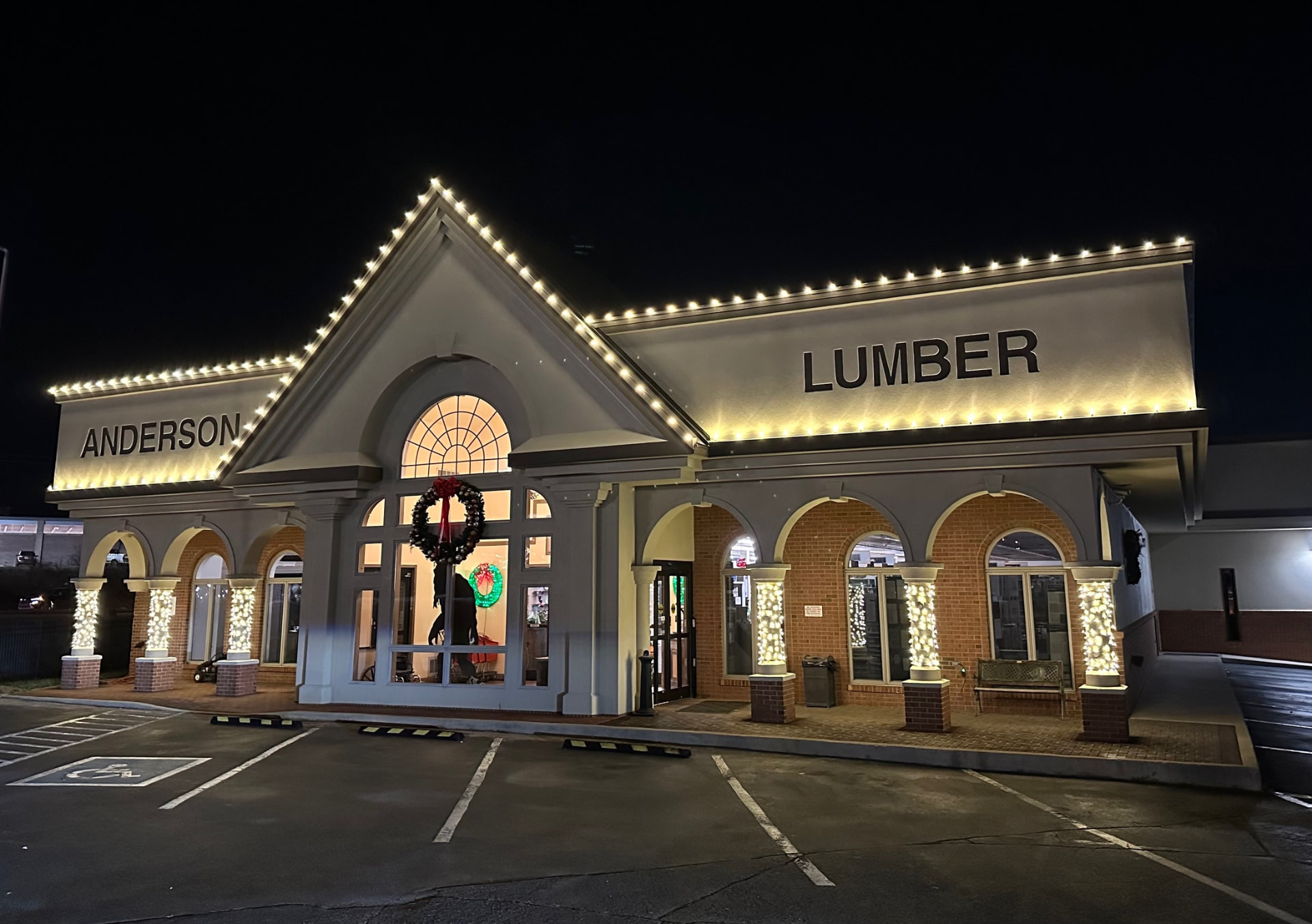 Anderson Lumber retail storefront in Maryville TN outlined in warm white C9 Christmas lights with wrapped brick columns and a lit wreath